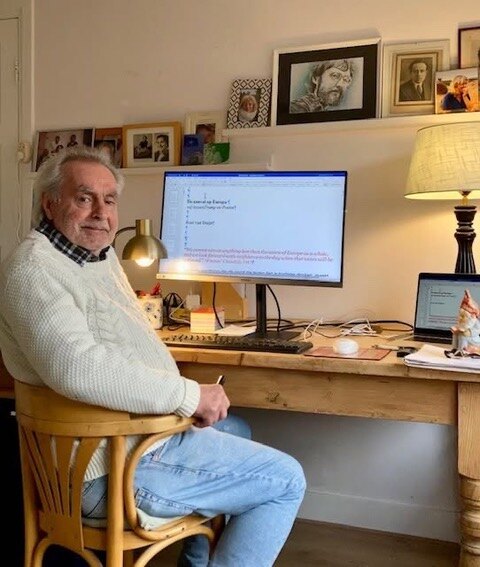 Roel van Duijn aan zijn bureau met een computer, in een witte trui