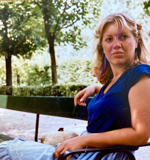Goedroen als jonge vrouw, in een blauw shirt op een bank in een park