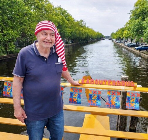 Roel van Duijn met een rood-witte kaboutermuts op een gele brug met het bord Kabouterbrug
